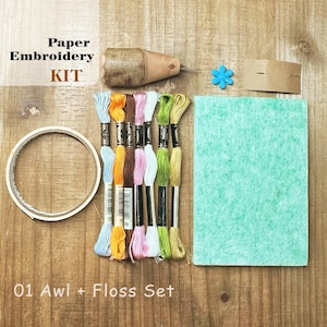 Puede incluir: Un kit de bordado en papel que incluye un punzón con mango de madera, un rollo de cinta blanca, seis madejas de hilo de bordar en azul, naranja, marrón, rosa, blanco y verde, una pequeña cuenta azul en forma de flor y fieltro verde.
