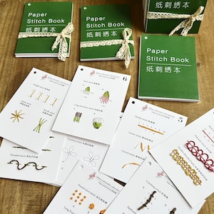May include: A selection of green paper stitch books with white lace ribbons and embroidery stitch guides. The guides show various embroidery techniques with diagrams and text, including French knot and Pekinese stitch.