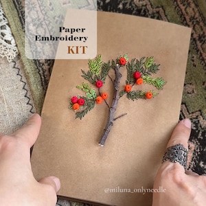 May include: A paper embroidery kit featuring a detailed embroidered tree design with red and orange berries and green leaves. The text "Paper Embroidery KIT" is displayed on the upper left corner. The artist's name, "@miluna_onlyneedle", is at the bottom.