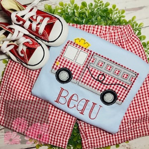 May include: A light blue t-shirt with a red and white gingham fire truck applique. The shirt has the name "Beau" embroidered on the front. The shirt is paired with red and white gingham shorts.