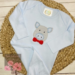 May include: A light blue baby onesie with a gray pig wearing a red bow tie embroidered on the front. The onesie has long sleeves and snaps at the crotch.