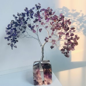 Könnte beinhalten: Eine handgefertigte Drahtbaumskulptur mit Blättern aus Amethyst-Edelsteinen. Der Stamm und die Äste des Baumes bestehen aus Silberdraht, und die Basis ist ein quadratischer Block aus lila und weißem Stein. Die Amethystblätter wechseln von tiefem Lila zu helleren Farbtönen.