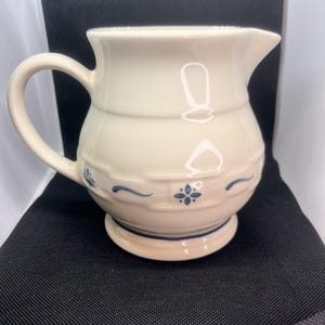 Puede incluir: Una taza de cerámica blanca con asa negra y el texto "But First, Coffee" en negro, con una fuente de estilo manuscrito. La taza está sobre una superficie blanca.