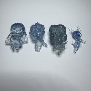 May include: Four small, translucent blue figurines arranged in a row. The set includes three human-like characters with distinct hairstyles and clothing, and one small deer-like creature with antlers. Each figure has a smooth, glossy finish.