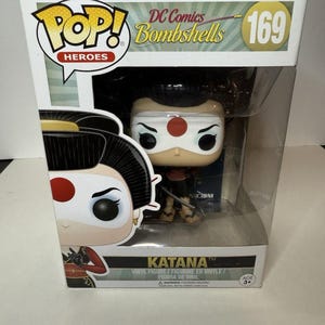 May include: A boxed Pop! Heroes vinyl figure of Katana from DC Comics Bombshells. The figure features a white blindfold, a red dot on the forehead, and a black and red outfit. The box displays the number 169.