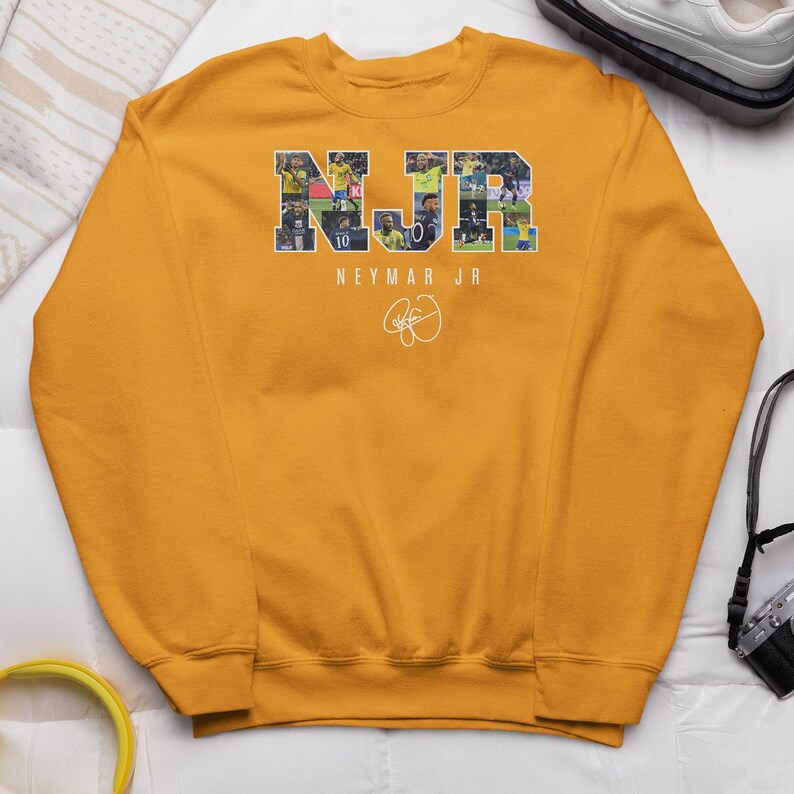 A yellow sweatshirt with the letters "NJR" printed on it, along with a signature, is displayed on a white surface.