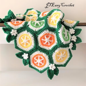 May include: A crocheted blanket with a citrus fruit design. The blanket is made of green, white, orange, and yellow yarn. The blanket is folded in half and has a white background.