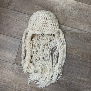 May include: A white crocheted hat with long, braided strands of yarn hanging down.