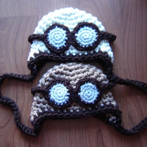 May include: Two crocheted hats with goggles. One hat is white with brown trim and the other is brown with white trim. Both hats have blue goggles.