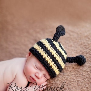 Può includere: Un neonato che indossa un cappello da ape a uncinetto a strisce nere e gialle con antenne. Il bambino sta dormendo su una superficie marrone e pelosa.