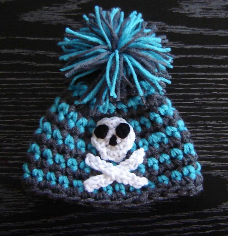 May include: A gray and turquoise crocheted hat with a white skull and crossbones design and a turquoise and gray pom-pom on top.