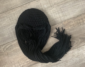 Puede incluir: Sombrero negro de ganchillo con flecos largos. El sombrero está hecho de hilo y tiene una superficie texturizada.