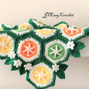 May include: A crocheted blanket with a green background and a pattern of orange, yellow, and white citrus fruit slices. The blanket has a border of green leaves and white flowers.