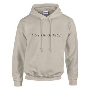 Könnte beinhalten: Hellbeige Kapuzenpullover mit Kordelzug und Fronttasche. Der Text "OUT OF OFFICE" ist schwarz auf die Brust gedruckt. Das Gildan-Markenetikett ist auf der Kapuze sichtbar.