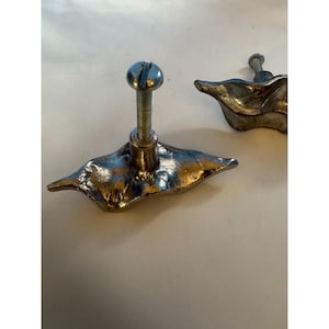May include: Two silver-toned metal cabinet knobs shaped like organic, irregular leaves. Each knob features a textured, metallic surface and includes a threaded bolt extending from the centre back for installation on furniture or cabinetry doors.