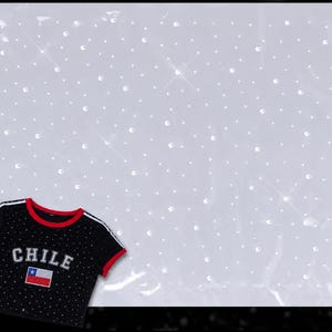 May include: A black short-sleeved t-shirt with red trim on the collar and sleeves, featuring white stripes on the shoulders, the word CHILE in white lettering, and a small Chilean flag graphic, all accented with scattered clear rhinestones.