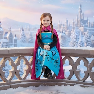 May include: A young girl in a blue and pink costume, reminiscent of a princess, sits on a snow-covered balcony. The costume features a blue dress with black floral designs and a pink cape. A castle is visible in the background.
