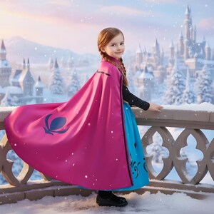 May include: A young girl in a pink cape and blue dress stands on a snowy balcony, with a castle in the background. The cape has a dark blue emblem and black trim. The dress has black and blue decorative elements.