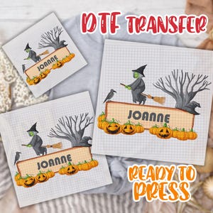 May include: A DTF transfer sheet featuring a Halloween design with a witch on a broomstick, a black crow, a bare tree, and a row of orange pumpkins. The design includes the name JOANNE in dark gray block letters on a light tan rectangular sign.