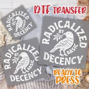 May include: Gray DTF transfer sheets with the text "RADICALIZED BY BASIC DECENCY" surrounding a dove holding an olive branch. The words "DTF TRANSFER" and "READY TO PRESS" are also visible.