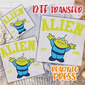 May include: DTF transfer sheets featuring a cartoon alien character in blue and green, with the word "ALIEN" in yellow. The design includes the text "EST 1995" and the words "READY TO PRESS".