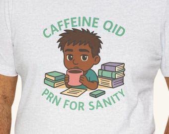May include: A light gray t-shirt featuring a cartoon illustration of a person drinking from a pink mug. The text "CAFFEINE QID" and "PRN FOR SANITY" are printed in green. Books are stacked around the person.