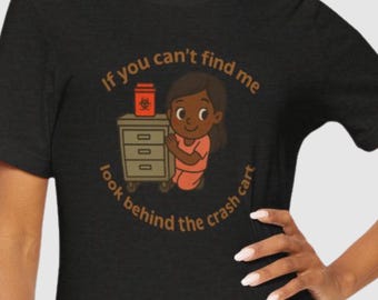 Pode incluir: Camiseta preta com um gráfico circular. O gráfico apresenta uma enfermeira de desenho animado com o texto "If you can't find me, look behind the crash cart."