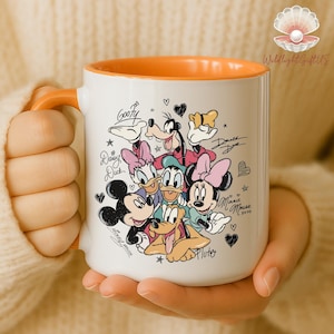 A person is holding a white mug with an illustration of Disney characters, including Mickey Mouse, Minnie Mouse, Donald Duck, Goofy, and Pluto.