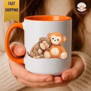 May include: White ceramic mug with an orange handle and interior. The mug features a cartoon illustration of two monkeys, one brown and sleeping, the other orange and plush. The mug has the text "FAST SHIPPING" in a yellow box.
