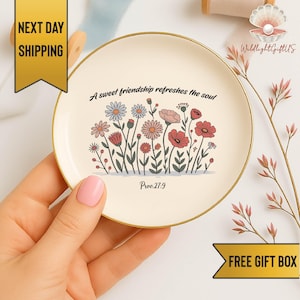 May include: A round, cream-colored trinket dish with a gold rim. The dish features a floral design with various flowers in pink, red, and blue. The text "A sweet friendship refreshes the soul" and "Prov.27:9" are also printed on the dish.
