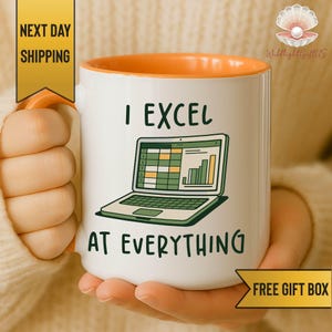 Peut inclure: Mug en céramique blanche avec intérieur et anse orange. Le mug affiche le texte "I Excel At Everything" avec un graphique d'un ordinateur portable affichant une feuille de calcul. Le mug est tenu par une personne.