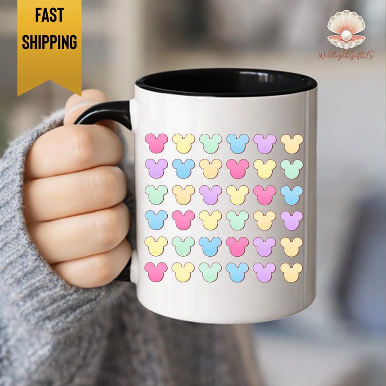 A person's hand holding a white mug with a colorful design of Mickey Mouse hearts on it.