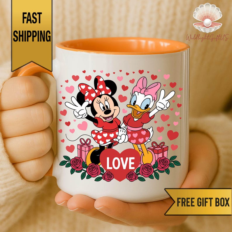 A person is holding a white mug with an illustration of Minnie Mouse and Donald Duck surrounded by hearts and flowers.