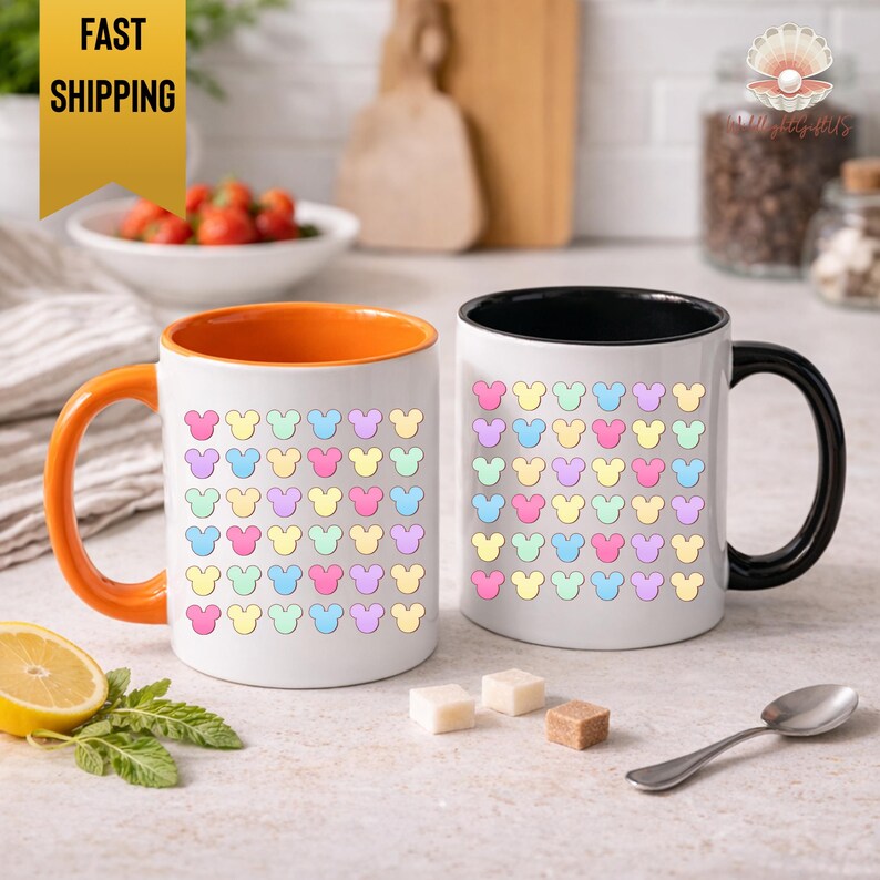 two colorful mugs with a playful Mickey Mouse pattern, placed on a kitchen counter with various food items and utensils in the background.
