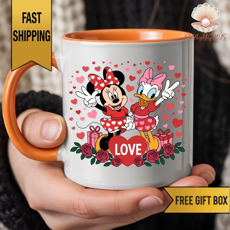 A person is holding a white mug with an illustration of Minnie Mouse and Donald Duck surrounded by hearts and flowers.