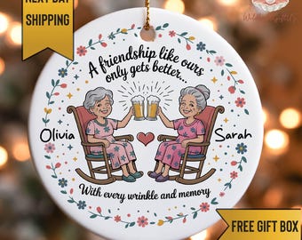 May include: A white ceramic ornament with a gold string for hanging. The ornament features two elderly women toasting beer mugs, with the names "Olivia" and "Sarah" on either side. Text reads "A friendship like ours only gets better..." and "With every wrinkle and memory."