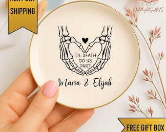 May include: A round, off-white ceramic trinket dish with a gold rim. The dish features a black graphic of skeleton hands forming a heart, with the text "TIL DEATH DO US PART" and the names "Maria & Elijah".