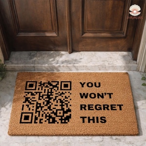 May include: A rectangular doormat made of natural coir fiber. The mat features a large QR code on the left and the words "YOU WON'T REGRET THIS" in black, centered on the right. The mat is placed in front of a wooden door.