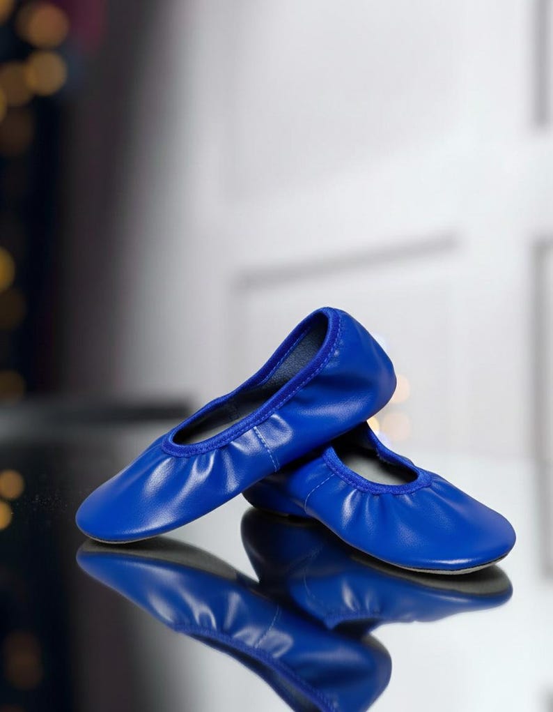 May include: A pair of vibrant blue ballet flats. These shoes have a rounded toe and a gathered vamp, with a smooth, shiny finish. The shoes are reflected in a glossy surface.