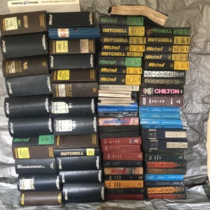 Puede incluir: Una colección de manuales de reparación de automóviles antiguos, incluidos títulos de Mitchell y Chilton. Los libros son de varios colores, con lomos negros, marrones y amarillos. Algunos manuales tienen texto visible, como "Mitchell" y "Chilton".