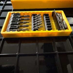 May include: A yellow tool organizer with various screwdriver bits and chisels. The organizer has multiple compartments holding different sizes and types of bits. The chisels have black and blue handles. The tools are arranged neatly, suggesting a focus on organization and efficiency.