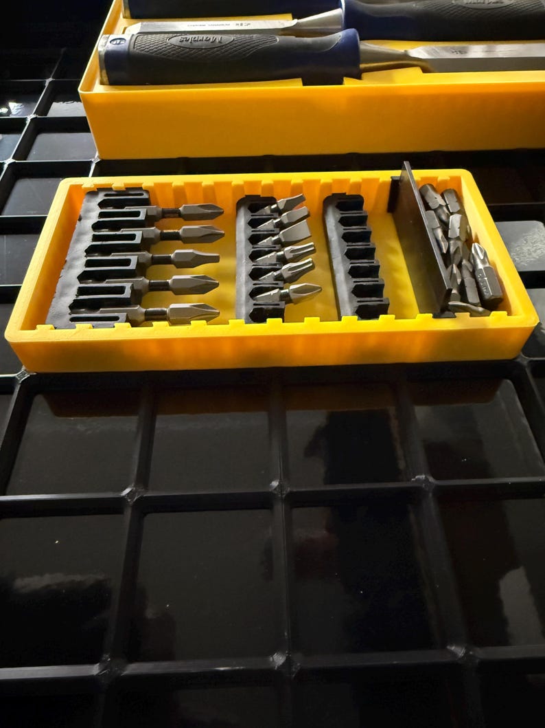 May include: A yellow tool organizer with various screwdriver bits and chisels. The organizer has multiple compartments holding different sizes and types of bits. The chisels have black and blue handles. The tools are arranged neatly, suggesting a focus on organization and efficiency.