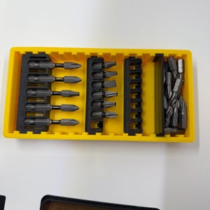 May include: A yellow plastic organizer filled with various dark gray screwdriver bits. The bits are arranged in black holders, showcasing different head types. The set includes a variety of sizes and shapes for diverse applications.