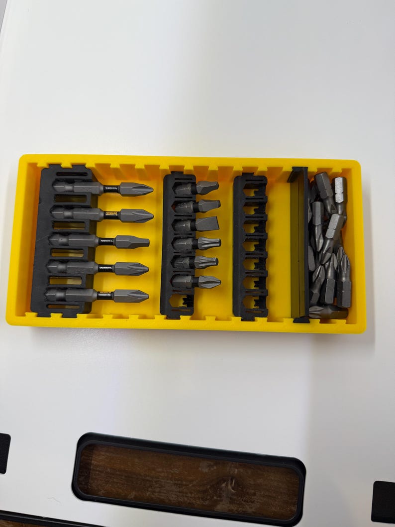 May include: A yellow plastic organizer filled with various dark gray screwdriver bits. The bits are arranged in black holders, showcasing different head types. The set includes a variety of sizes and shapes for diverse applications.