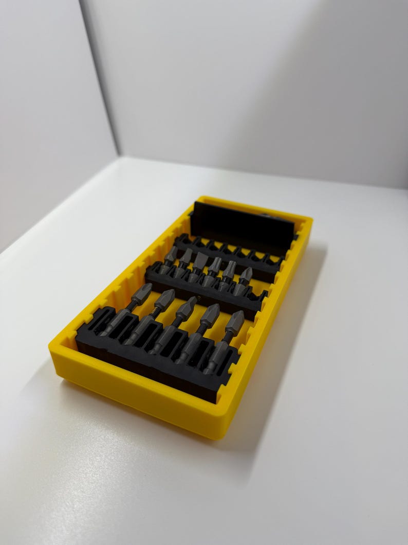 May include: A yellow plastic case containing a set of black screwdriver bits. The bits are arranged in rows within the case. The case is rectangular and has a slightly textured surface.