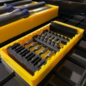 May include: A set of various screwdriver bits and chisels in yellow plastic cases. The chisels have blue and black handles. The bits are silver and black. The tools are organized in a black metal toolbox.