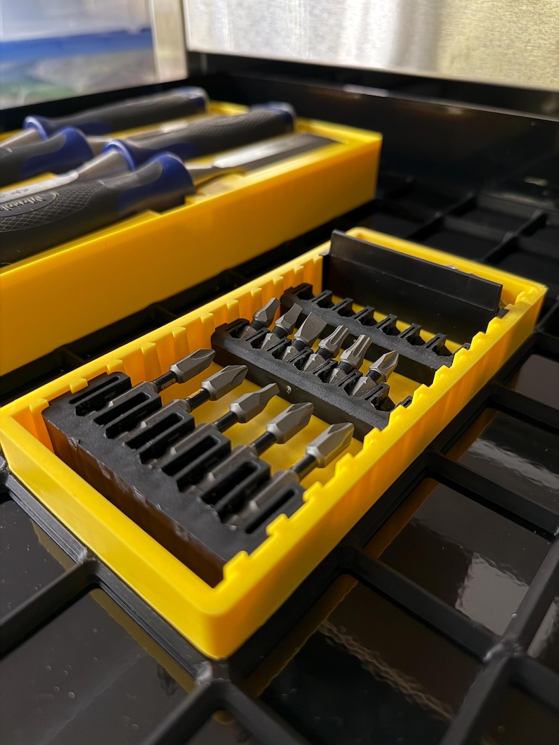May include: A set of various screwdriver bits and chisels in yellow plastic cases. The chisels have blue and black handles. The bits are silver and black. The tools are organized in a black metal toolbox.