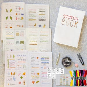 Pode incluir: Um kit de bordado com um "Stitch Book" com letras bordadas, guias de pontos abertos, agulhas, tesouras e fios de bordar coloridos. As páginas do livro exibem vários exemplos de pontos.