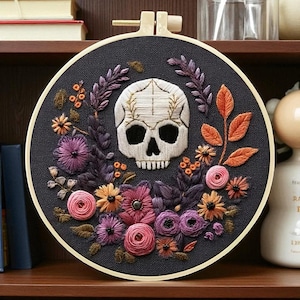 Peut inclure: Broderie artisanale dans un cercle, représentant un crâne blanc entouré de fleurs roses, violettes, oranges et jaunes. Le fond est gris foncé. Une décoration murale originale et colorée.