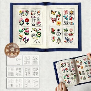 Puede incluir: Un libro de bordado abierto con coloridos diseños florales y de animales. El libro presenta una cubierta azul y contiene varios patrones bordados de flores, mariposas y criaturas del bosque. También se ven un libro más pequeño y una pegatina circular.